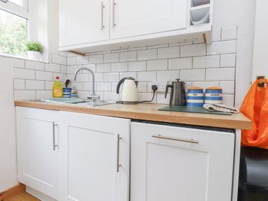 A kitchen countertop with a sink kettle tea and sugar containers at 3 Glyn Y Mor in Llanbedrog