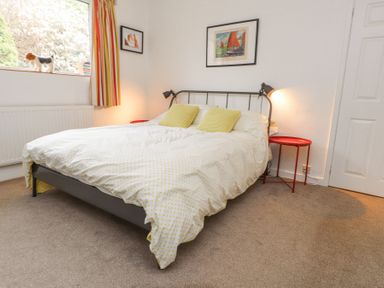 A bedroom with a bed with yellow pillows and polka dot bedding two red bedside tables and framed pictures on the wall at 3 Glyn Y Mor in Llanbedrog