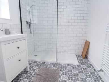 A bathroom with a walk-in shower a white vanity with two drawers and patterned floor tiles at 3 Glyn Y Mor in Llanbedrog