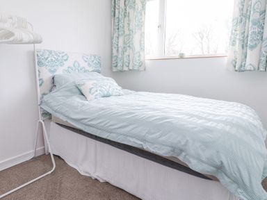 A bedroom with a single bed next to a window and a white clothes rack at 3 Glyn Y Mor in Llanbedrog