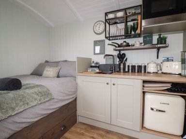 A small kitchen area with countertop appliances next to a bed with gray bedding at The Highwood Hut near Liskeard