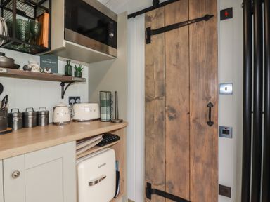 A kitchen corner with a wooden countertop microwave toaster kettle canisters shelving and a wooden door at The Highwood Hut near Liskeard