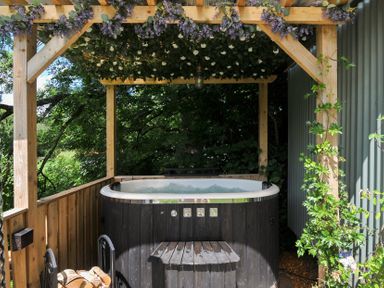 An outdoor hot tub surrounded by wood and plants at The Highwood Hut near Liskeard