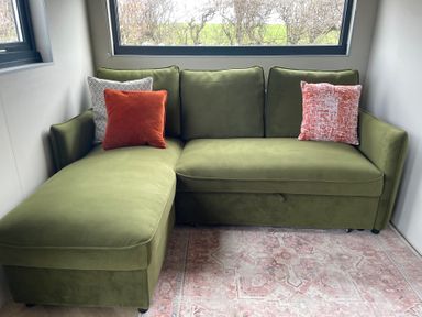 A green sectional sofa with three cushions near two windows at Caban in Dothan near Gwalchmai