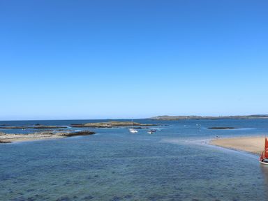 A coastal scene with rocky islands and boats on water at Caban in Dothan near Gwalchmai