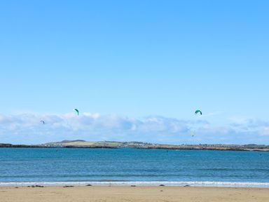 A beach with blue water and kite surfers in the distance at Caban Dothan near Gwalchmai