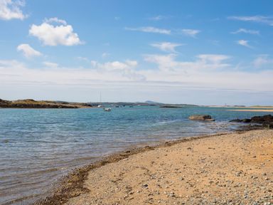 A beach with pebbles and a rocky shoreline with boats in the water at Caban in Dothan near Gwalchmai