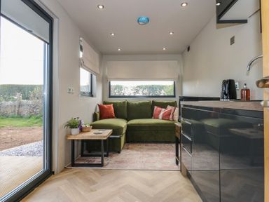 A small living area with a green sofa and two side tables next to a kitchen unit at Caban in Dothan near Gwalchmai