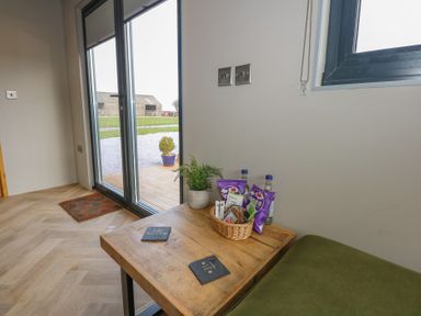 A corner of a room with a wooden table holding snacks and a plant next to glass patio doors and a window at Caban in Dothan near Gwalchmai