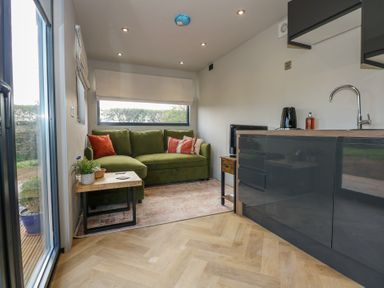 A living area with green sofa orange pillows side table and kitchen area with sink at Caban in Dothan near Gwalchmai