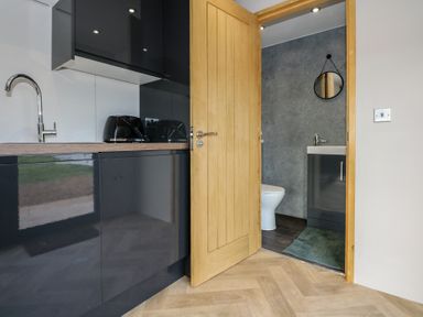 A kitchen area with black cabinets and a toaster next to an open door leading to a bathroom with a toilet and sink at Caban in Dothan near Gwalchmai