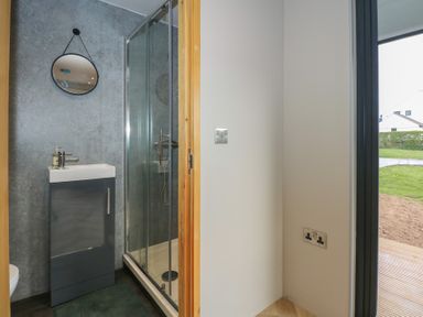 A bathroom with a shower enclosure a small sink with cabinet and a round mirror at Caban in Dothan near Gwalchmai