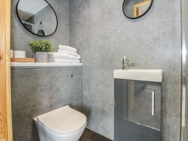 A bathroom with a wall-mounted toilet a sink with cabinet a round mirror and towels at Caban in Dothan near Gwalchmai