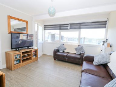 A living room with two brown leather sofas next to windows with blinds and a television on a wooden stand with a mirror above at Chalet 38 in Hemsby