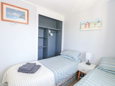 A bedroom with two single beds striped bedding a nightstand with a lamp an open closet and framed pictures on the wall at Chalet 38 in Hemsby