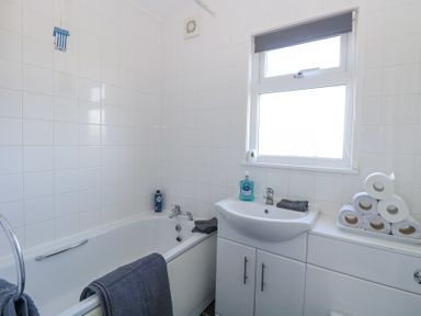 A bathroom with a bathtub a sink a window and toilet rolls stacked on a cabinet at Chalet 39 in Hemsby