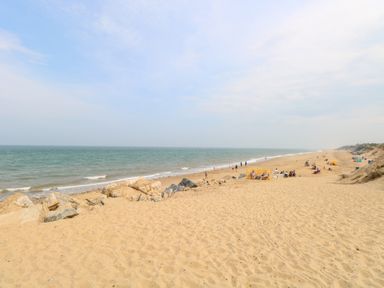 A sandy beach with people sitting and walking near the sea at Chalet 39 in Hemsby