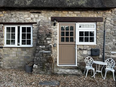 An outdoor area with stone wall, door, window, table and chairs at Bracken Cottage