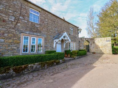 Exterior stone wall of a house with windows a white door with a small porch cobblestone pathway and trimmed hedges at Pagecroft Cottage in Haydon Bridge