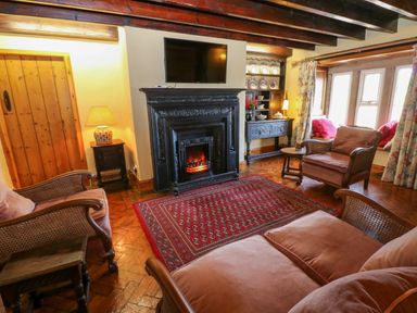 A living room with wooden beams a fireplace sofa armchairs a red rug and a window seat at Pagecroft Cottage in Haydon Bridge