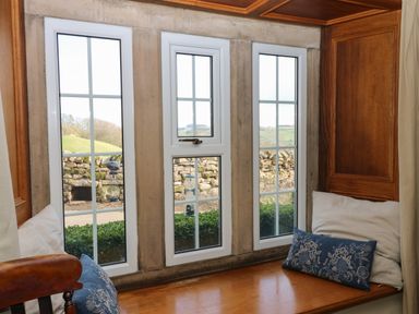 A window seat with cushions and a view of a stone wall and countryside at Pagecroft Cottage in Haydon Bridge