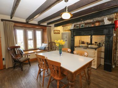 A dining room with a wooden table and chairs a vintage stove and window seating at Pagecroft Cottage in Haydon Bridge