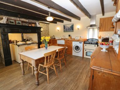 A kitchen with wooden cabinets dining table chairs stove and washing machine at Pagecroft Cottage in Haydon Bridge