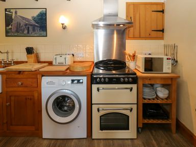 A kitchen with a washing machine stove microwave wooden countertops and shelves at Pagecroft Cottage in Haydon Bridge