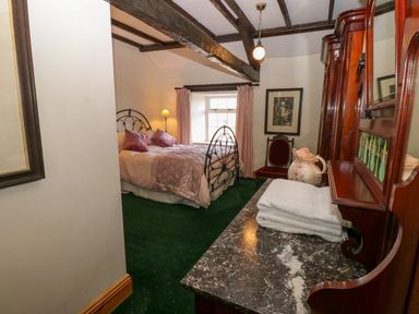 A bedroom with a bed pillows curtains a chair wooden furniture and folded towels at Pagecroft Cottage in Haydon Bridge