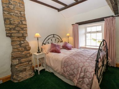 A bedroom with a metal bed frame pink bedding and two lamps next to a window at Pagecroft Cottage in Haydon Bridge