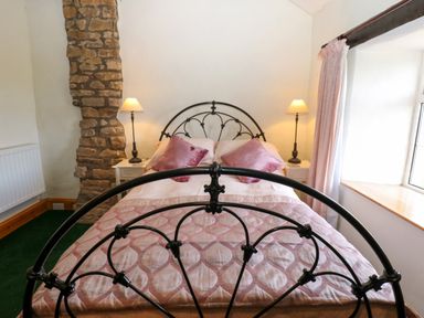 A bedroom with a black metal bed frame pink pillows a stone wall feature and two lamps at Pagecroft Cottage in Haydon Bridge