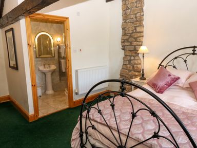 A bedroom with a metal bed frame pink bedding stone wall lamp and an open doorway to a bathroom at Pagecroft Cottage in Haydon Bridge
