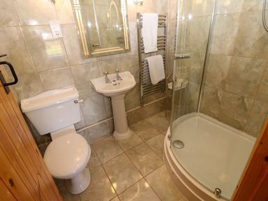 A bathroom with a toilet sink mirrored cabinet curved glass shower door heated towel rail and tiled floors at Pagecroft Cottage in Haydon Bridge