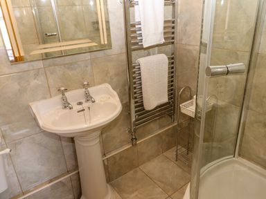 A bathroom with a pedestal sink a mirror towel rack with towels and a glass enclosed corner shower at Pagecroft Cottage in Haydon Bridge