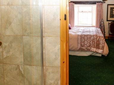 A bathroom with beige tiled shower next to a bedroom with a bed and window at Pagecroft Cottage in Haydon Bridge