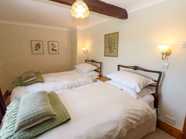 A bedroom with two single beds wooden headboards green cushions and framed floral pictures on the walls at Pagecroft Cottage in Haydon Bridge