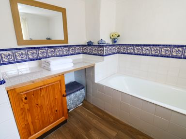 A bathroom with a wooden cabinet white tiles blue decorative tile border and a bathtub at Pagecroft Cottage in Haydon Bridge