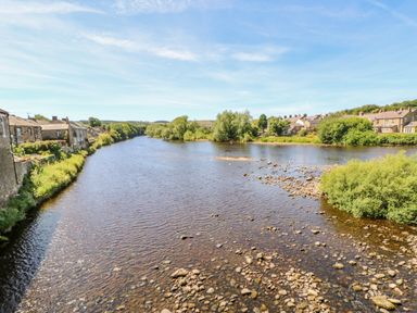 A river with stones in the water and houses along the banks at Pagecroft Cottage in Haydon Bridge