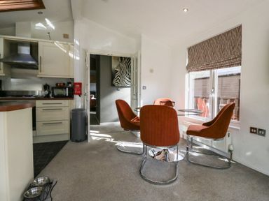 A dining area with four orange chairs around a round table next to a window and a kitchen area with white cabinets