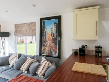 A kitchen and living area with a grey sofa and decorative pillows next to a wooden counter with a cutting board at Gressingham View Lodge Dock Acres near Carnforth