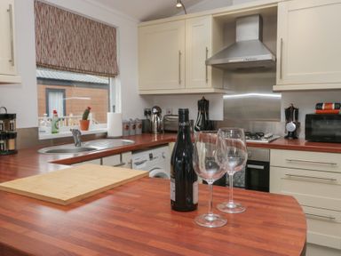 A kitchen with wooden countertops white cabinets a sink a wine bottle two wine glasses and kitchen appliances at Gressingham View Lodge Dock Acres near Carnforth