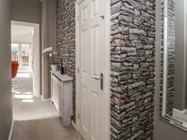 A hallway with stone-patterned wallpaper a white door a radiator cover with white flowers a mirror and a view into a room with chairs at Gressingham View Lodge Dock Acres near Carnforth