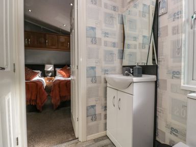 A bathroom with a white sink and mirror looking into a bedroom with two single beds and wooden cabinets at Gressingham View Lodge Dock Acres near Carnforth