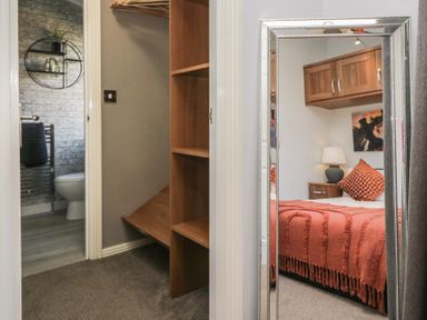 View of a bathroom with toilet and towel rack through a doorway and a mirror reflecting a bedroom with bed lamp and wooden cabinets at Gressingham View Lodge Dock Acres near Carnforth