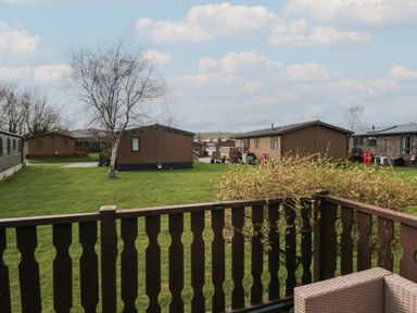 A view of wooden lodges on grassy land with a tree and wooden fence railing at Gressingham View Lodge in Dock Acres near Carnforth