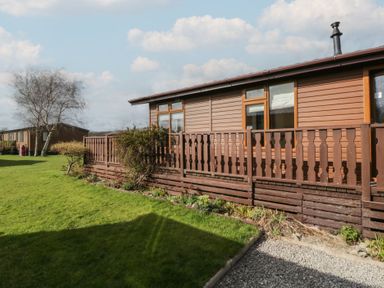 A wooden lodge with a brown fence and green grass outside at Gressingham View Lodge Dock Acres near Carnforth
