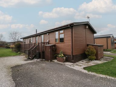 A brown wooden lodge with stairs and a small garden area at Gressingham View Lodge in Dock Acres near Carnforth