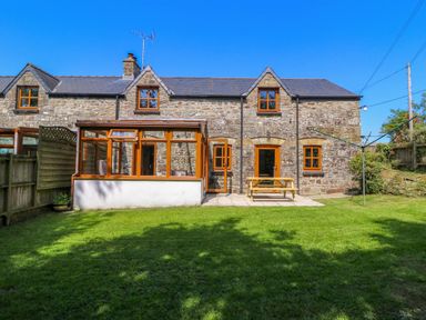 A stone house with wooden framed windows and a conservatory overlooking a grass garden at Cove Cottage in Llangrannog