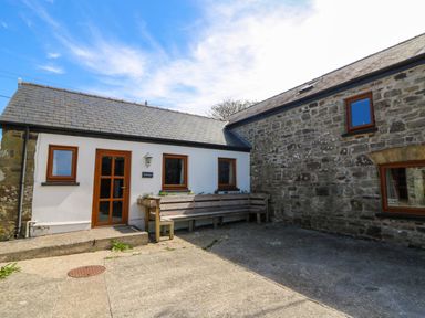 An exterior courtyard with stone and white walls wooden windows and a wooden bench at Cove Cottage in Llangrannog