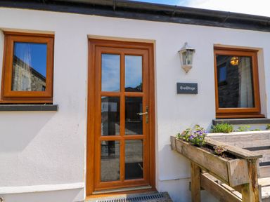 Cottage exterior with wooden door and two windows and a planter with flowers at Cove Cottage in Llangrannog
